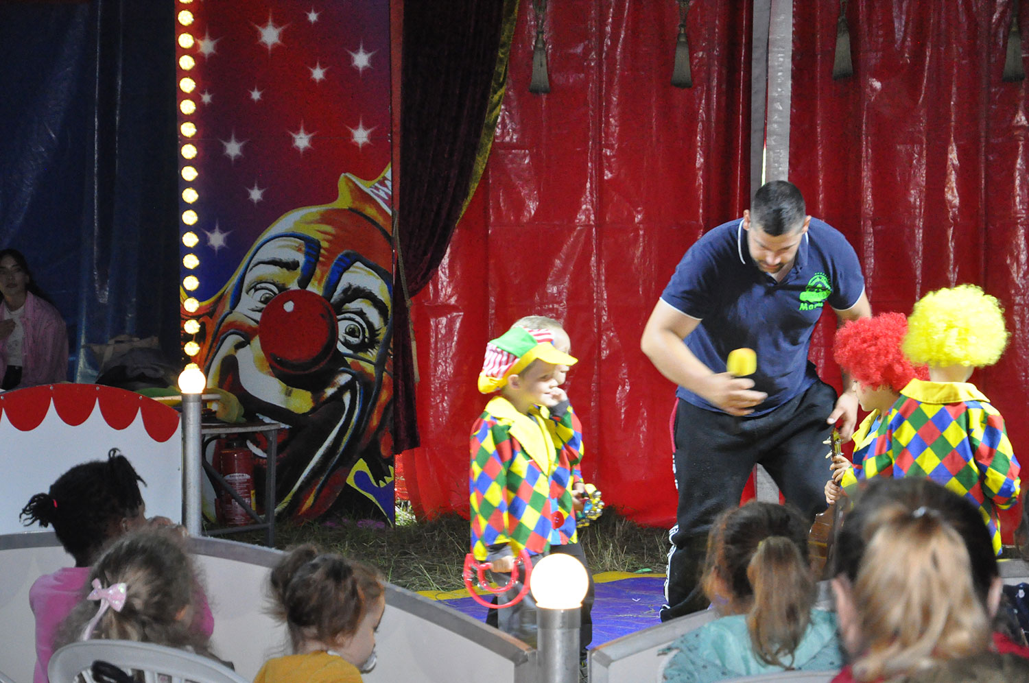 Zwei Kinder im Clownskostüm stehen in der Manege und werden von einem Moderator befragt